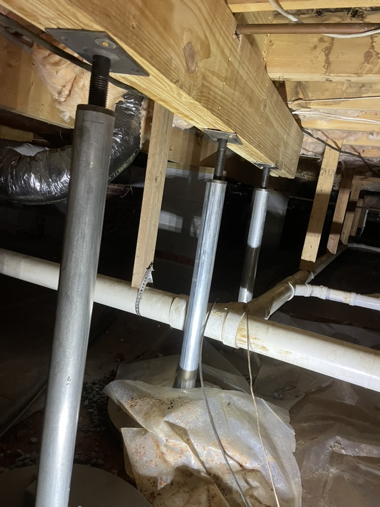 Adjustable steel post jacks on a beam in an Upstate Crawlspace